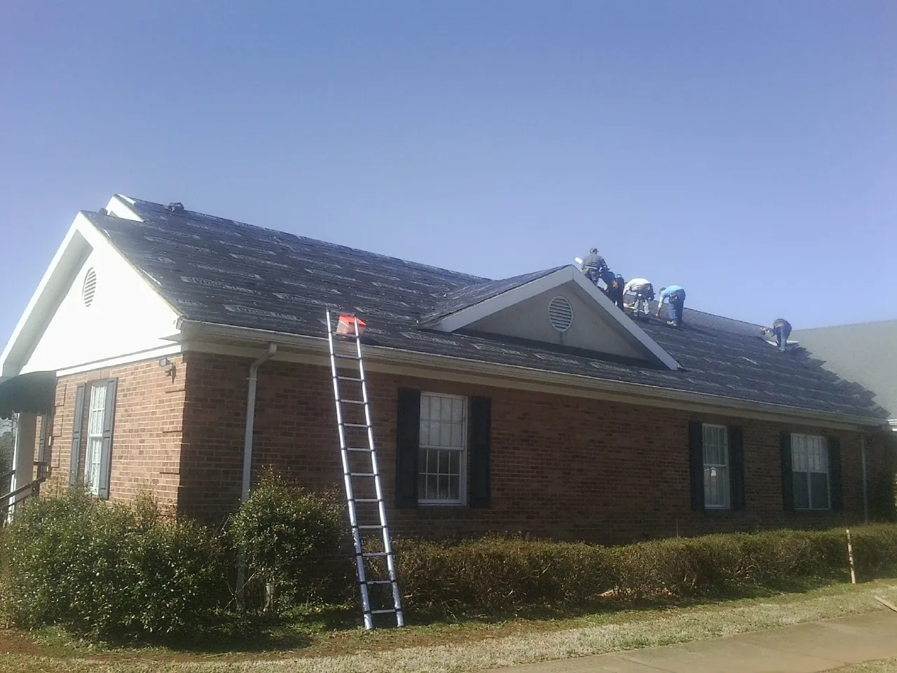Crew tearing shingles off a brick ranch roof with a ladder set — Metal Roof Repair work by our crew in East Haddam