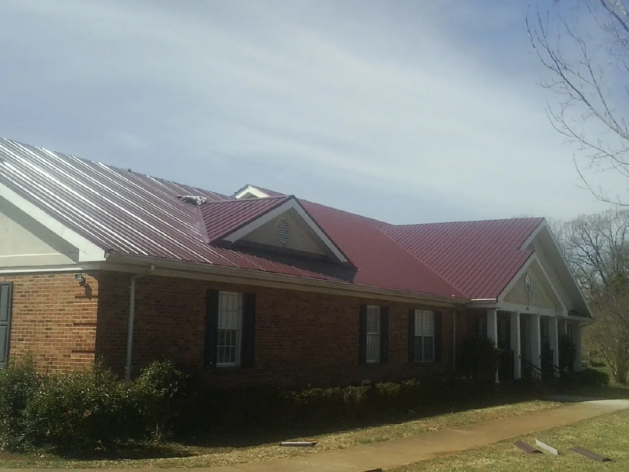 Red metal roof with gabled entries on a long brick building, from a Hail Damage Roof Repair job in East Haddam