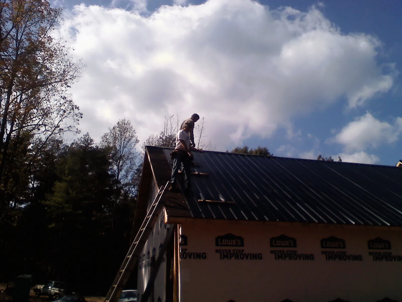 Roofer fastening dark metal panels high against a cloudy sky, from a Roof Inspection job in East Haddam