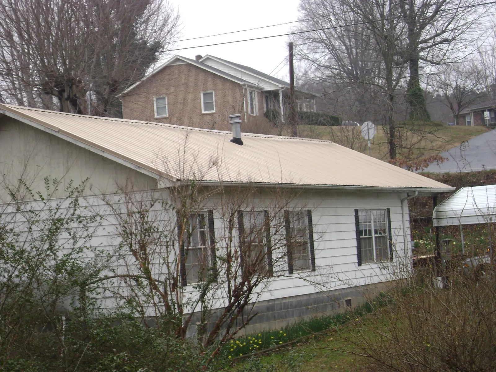 Tan metal roof on a white sided house set into a hillside — Commercial Roofing by Roofing Brothers in East Haddam